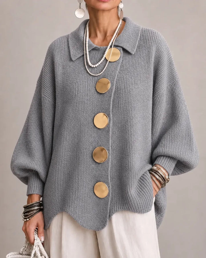 Medium gray ribbed cardigan worn by a model, featuring five gold buttons, layered pearl necklaces and white trousers. 18