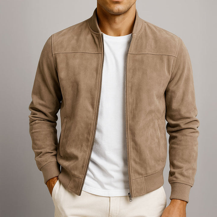Model wearing the tan faux suede bomber unzipped over a white tee and cream chinos, one hand in pocket.
