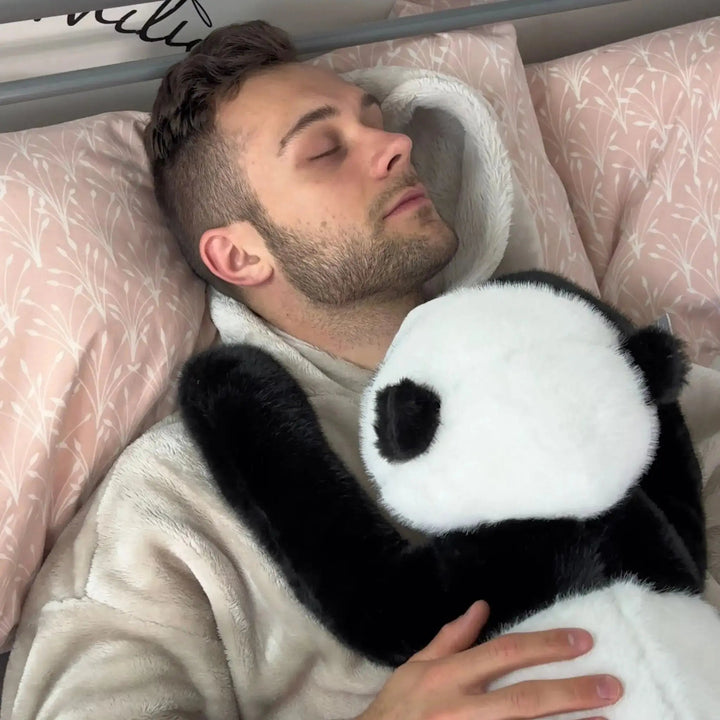 Man asleep in bed with the panda plush tucked against his chest, its black arm resting over his shoulder. 11