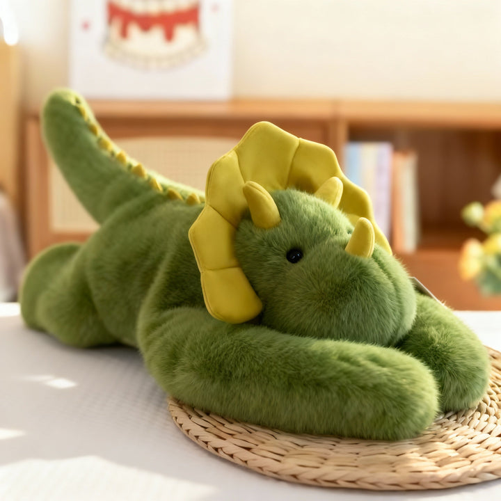 Green dinosaur plush with a yellow frill and small horns lying on a woven straw mat, long arms folded in front. 15