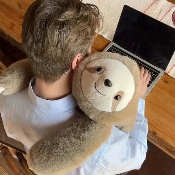 Overhead view of a man working on a laptop with a sloth plush hugging his neck and shoulders. 9