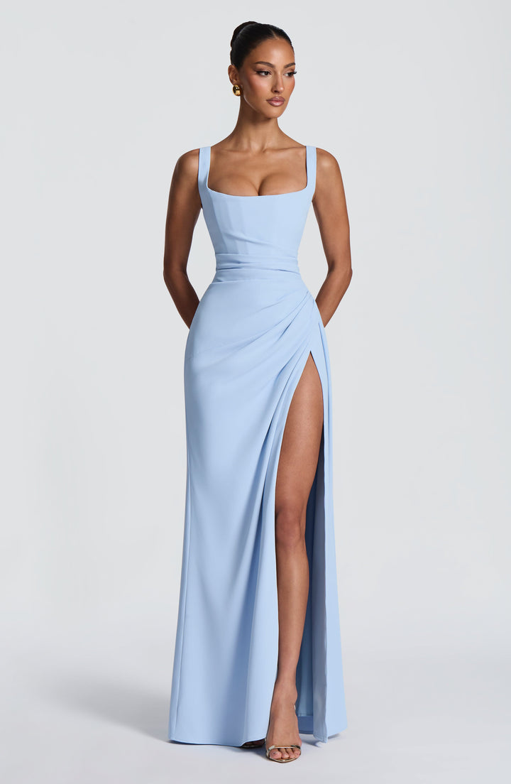Model standing front view in the light blue gown with square neckline, ruched waist and a high slit revealing her leg. 24