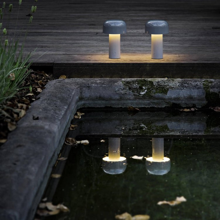 Two lit mushroom lamps on a wooden deck by a dark pond, reflected in the water 13
