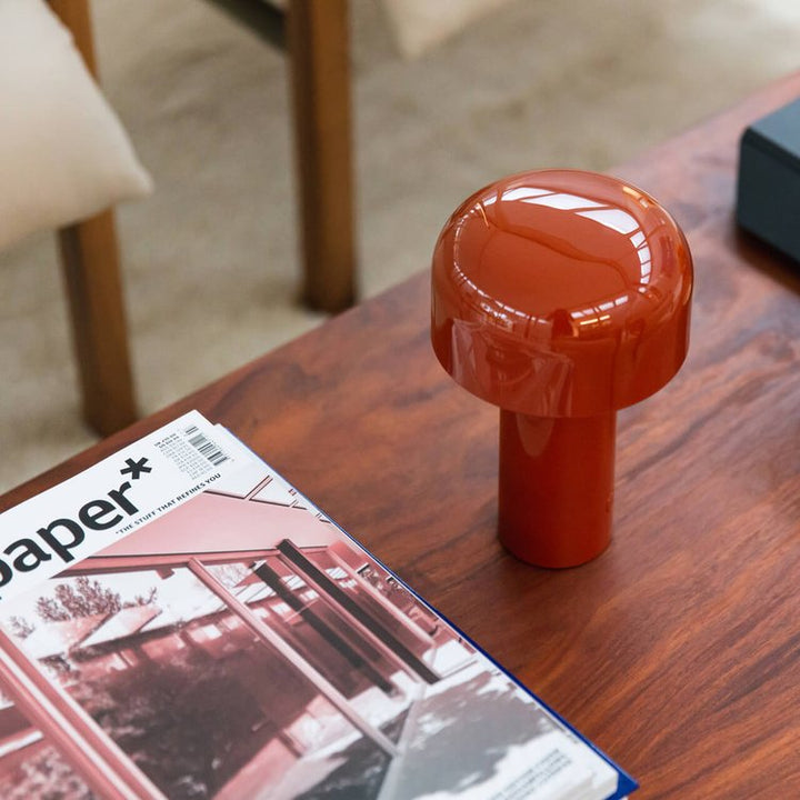 Glossy red lamp on a wooden coffee table next to an open magazine, seen from above 14