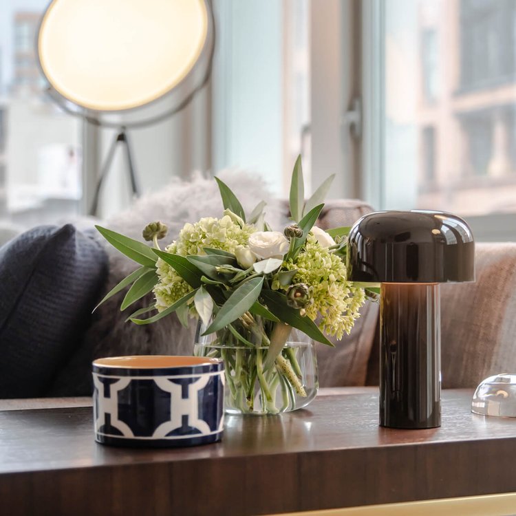Black glossy lamp on a wooden table beside a bouquet of white flowers and a patterned bowl 16