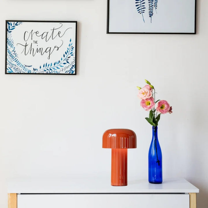 Orange lamp on a white dresser next to a blue glass vase of pink flowers and framed prints 19