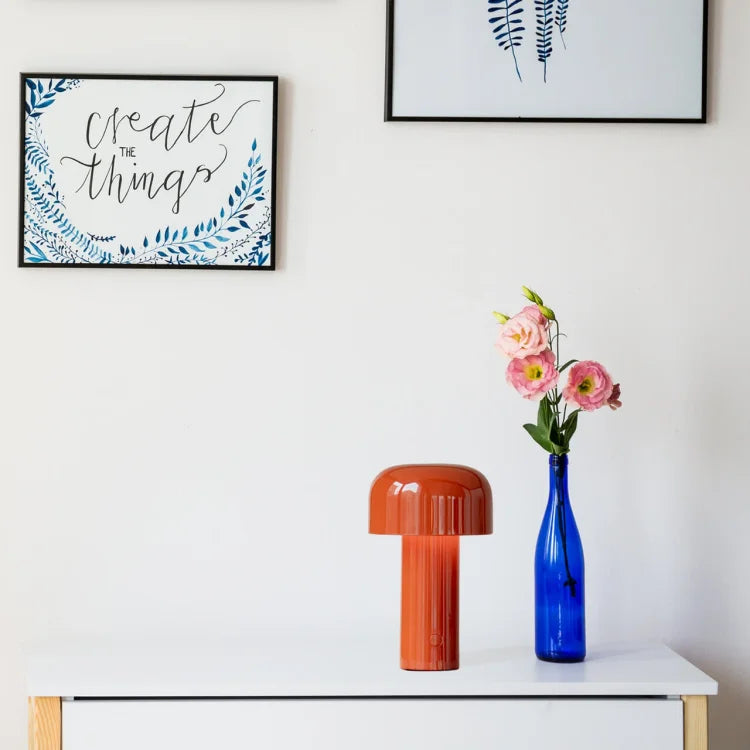 Red-orange mushroom lamp on a white dresser beside a blue bottle holding pink flowers 20