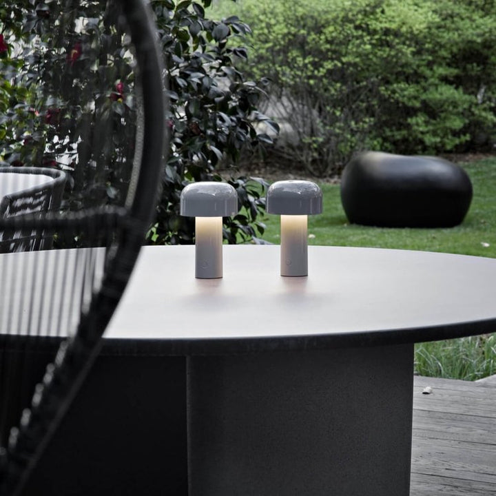 Pair of gray mushroom lamps lit on a round outdoor table with garden behind 23