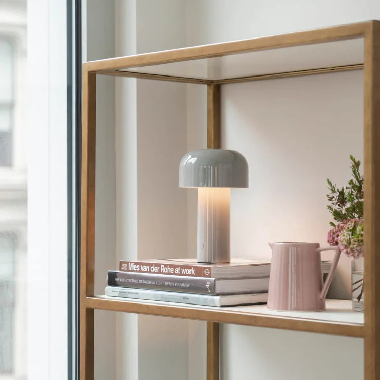 Gray mushroom lamp glowing on a stack of books on a shelf beside a pink pitcher 23