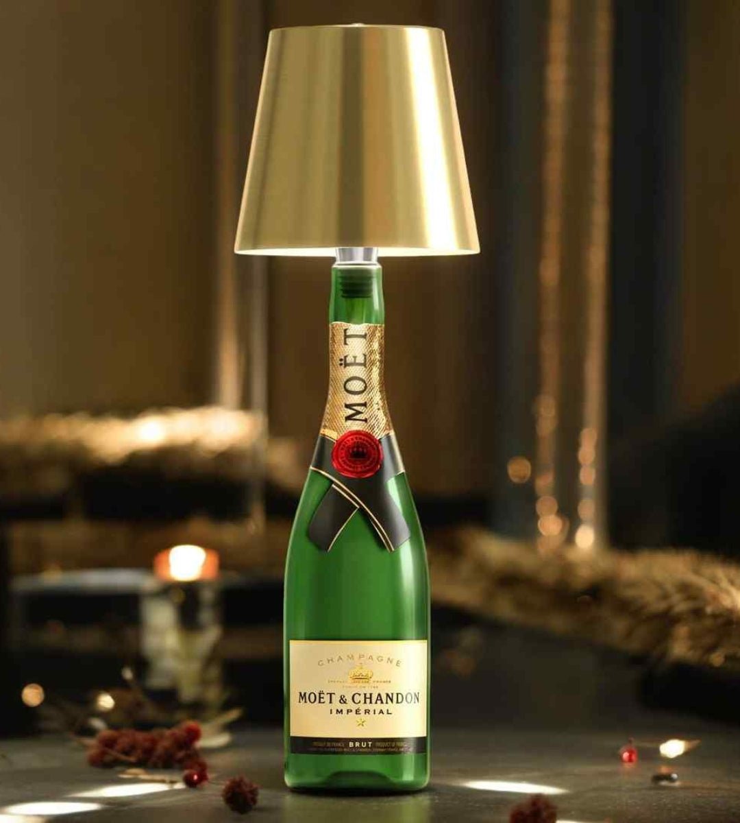 Gold bottle lamp on a green champagne bottle, glowing warmly on a dark table.