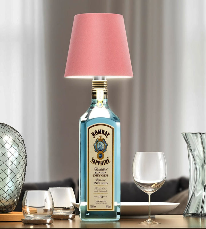 Pink bottle lamp on a blue gin bottle on a dining table.