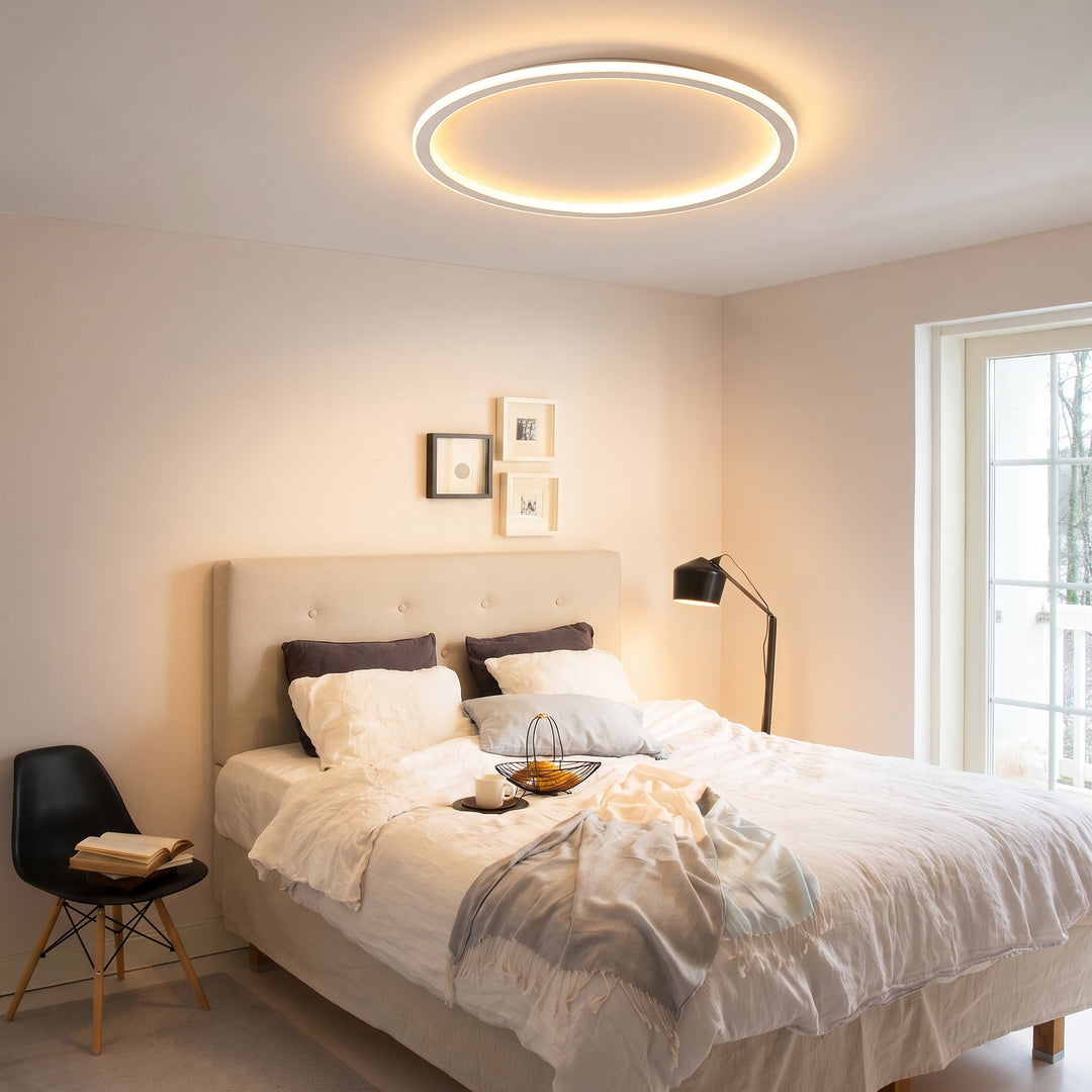 White ring ceiling light glowing over a bedroom with a tufted beige headboard
