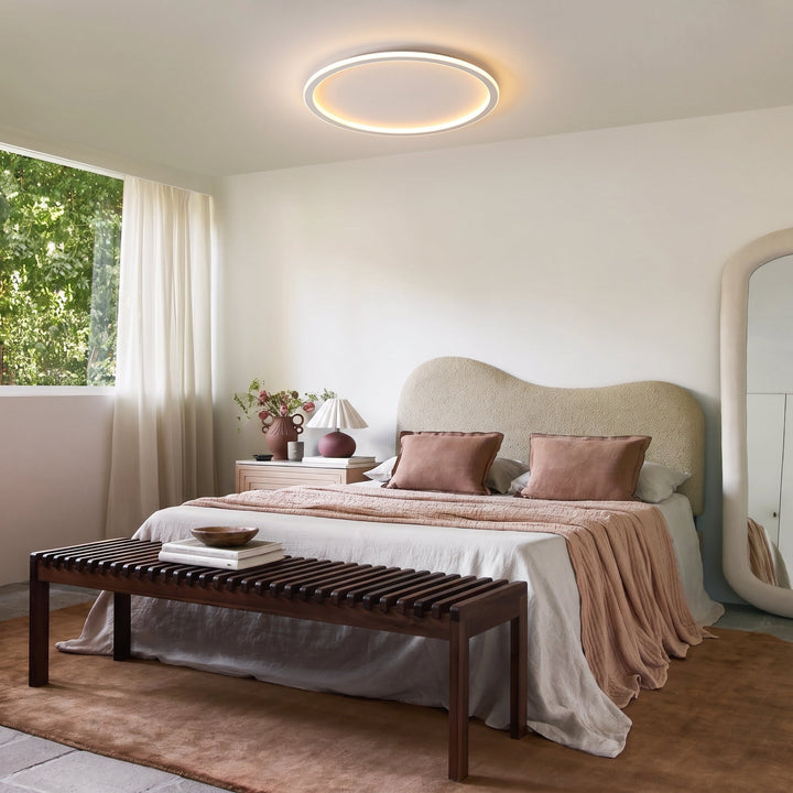 White round LED ceiling light above a bedroom with a curved boucle headboard