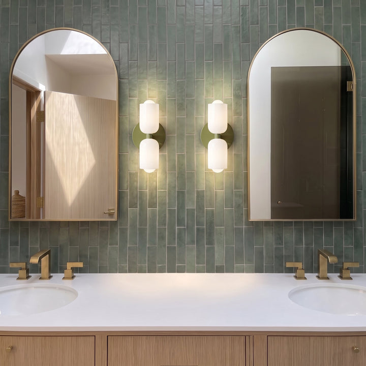 Pair of olive green wall lights with white glass shades flanking tall arched mirrors above brass faucets on a green-tiled bathroom vanity. 7