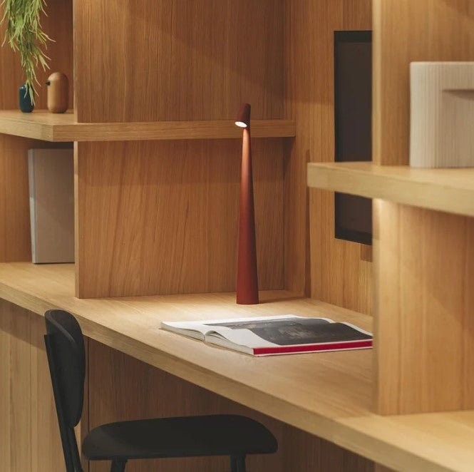Another view of a terracotta red rechargeable LED table lamp lighting an open magazine on a desk.