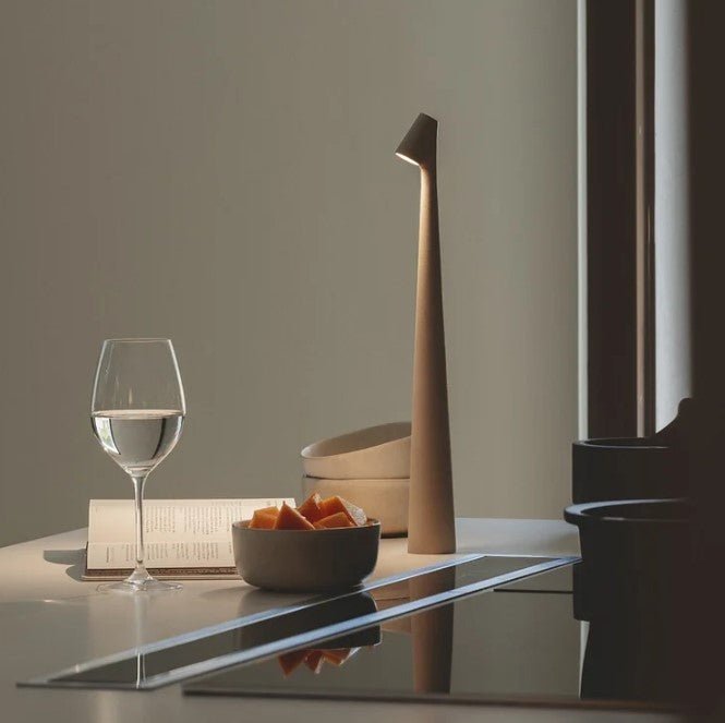 Another view of a tan rechargeable LED table lamp lit on a kitchen counter beside a wine glass.
