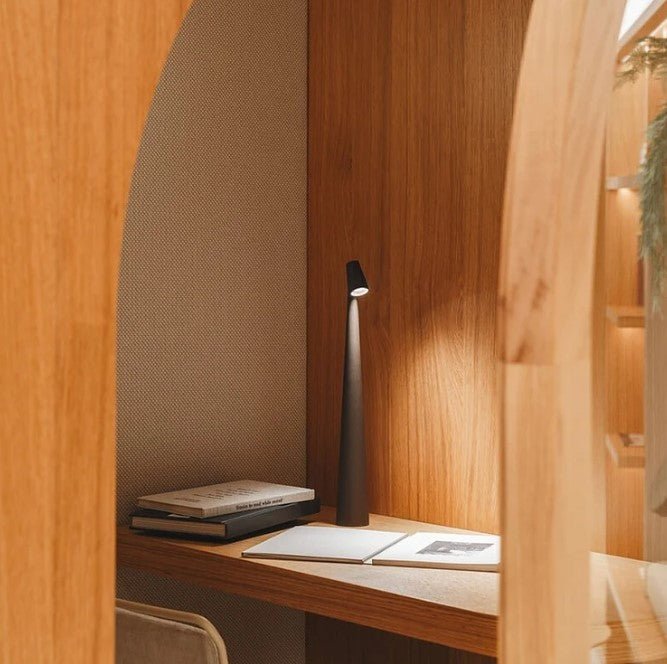 Another view of a dark rechargeable LED table lamp lit on a wooden desk inside an arched alcove.