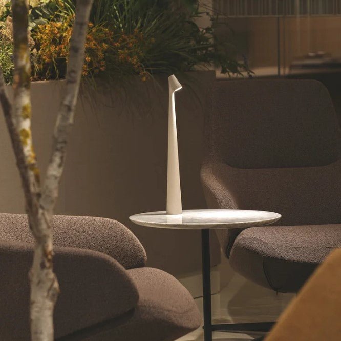 Another view of a white rechargeable LED table lamp on a marble side table between armchairs.