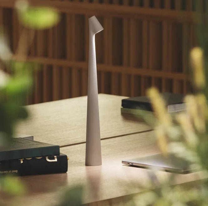 Another view of a light grey rechargeable LED table lamp glowing on a wooden desk.