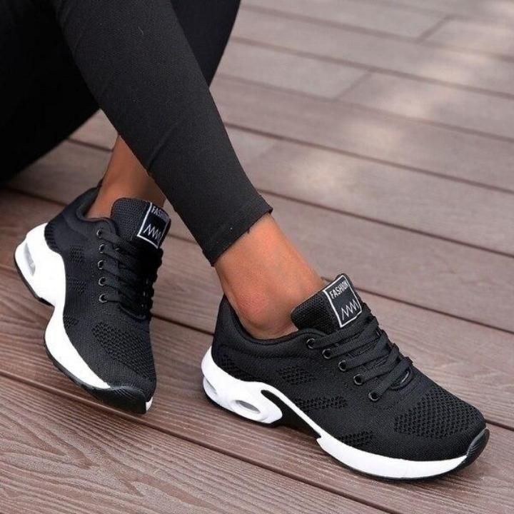 Black mesh lace-up sneakers with a white cushioned sole and air window, worn with black leggings on a wooden deck. 1