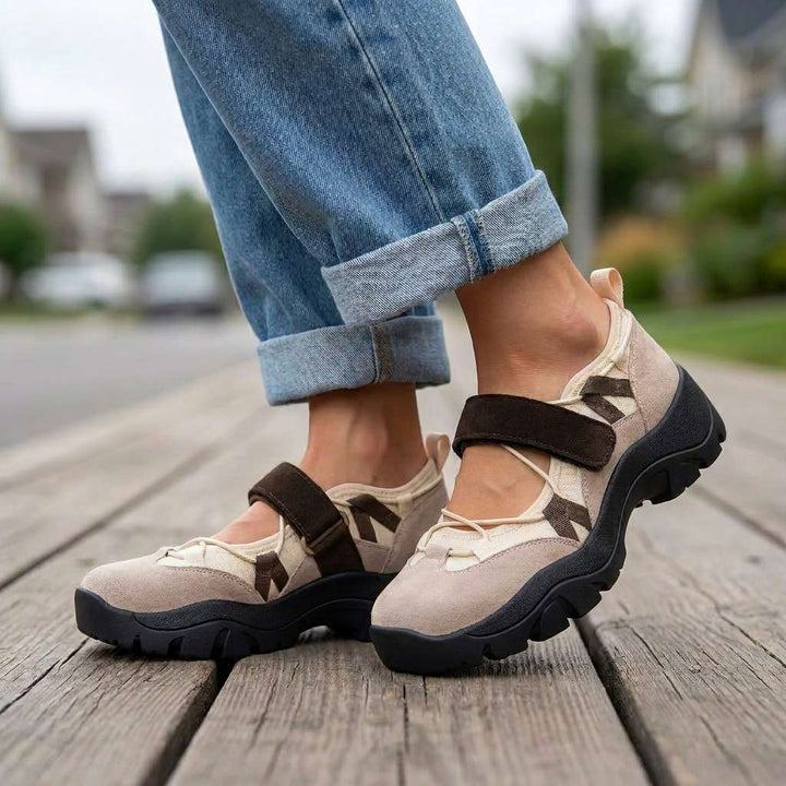 Beige suede shoes with dark brown straps and black chunky soles, worn with cuffed jeans on a wooden boardwalk outdoors. 6