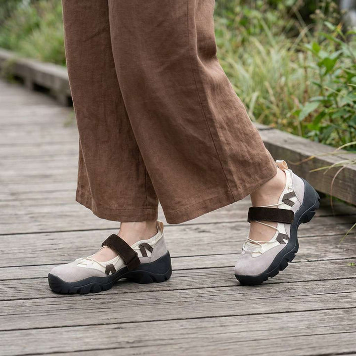 Beige strap shoes with brown straps and dark soles, worn with wide-leg brown linen pants on a wooden boardwalk. 11