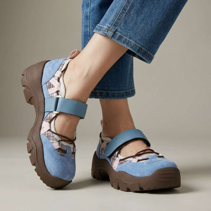 Blue suede strap shoes with plaid panels, pink accents and a chunky brown sole, worn with light-wash jeans in a studio. 3