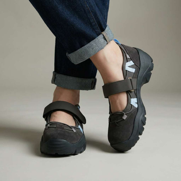 Dark gray strap shoes with light blue accent laces and chunky black soles, worn with cuffed dark jeans in a studio. 2