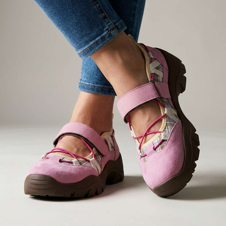 Pink suede strap shoes with bright pink elastic laces, plaid inserts and a chunky brown sole, worn with blue jeans in a studio. 4