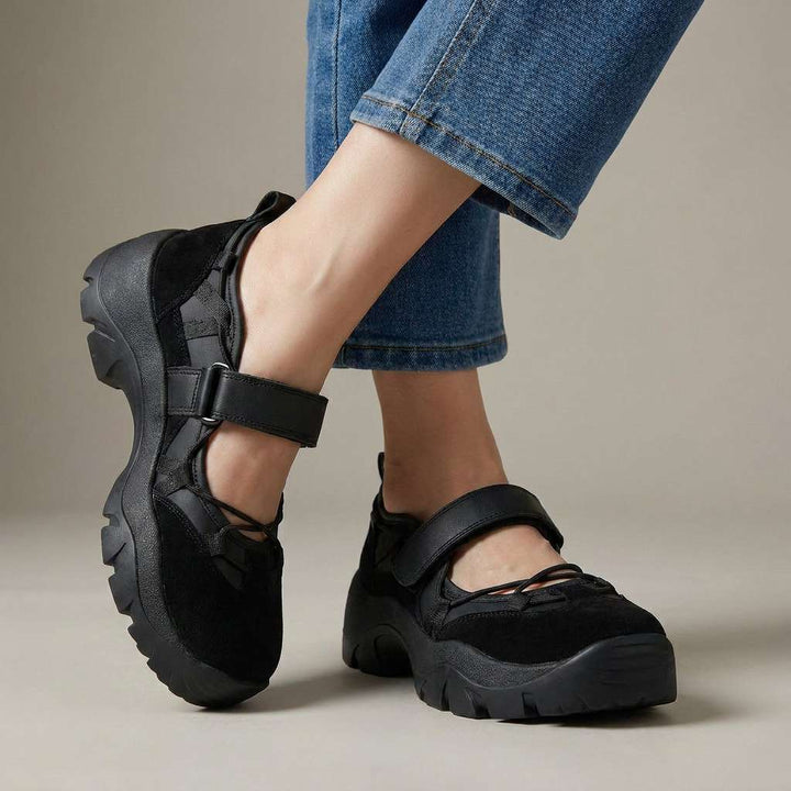 All-black suede strap shoes with a thick lugged sole, worn with straight-leg blue jeans against a neutral studio background. 5