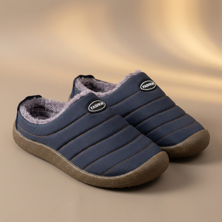 Pair of navy blue quilted slippers with gray fleece lining on a soft beige studio backdrop 18