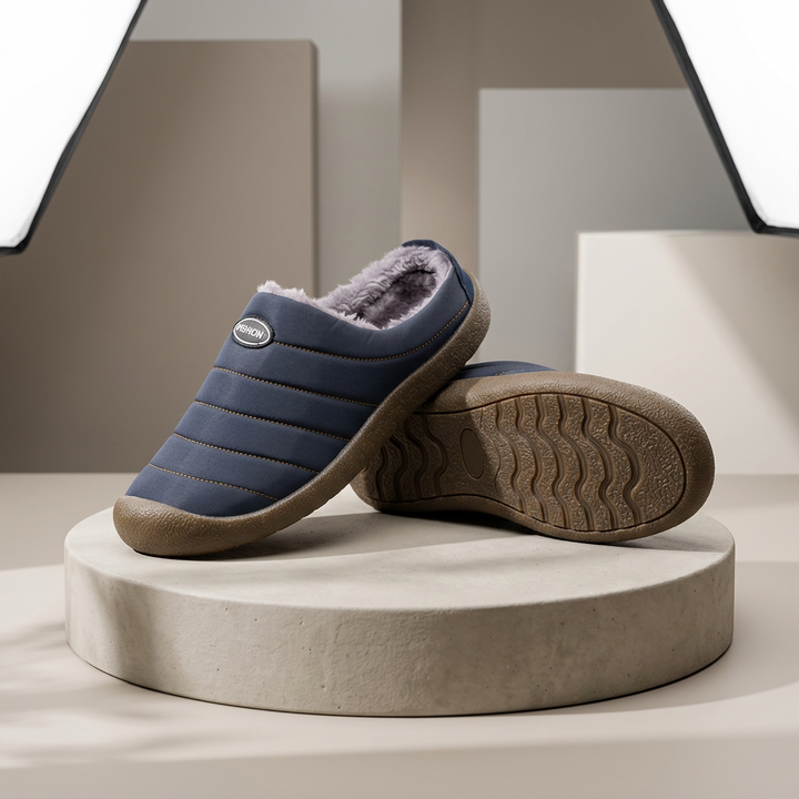 Navy quilted slippers with gray fleece lining, one resting on its side to show the wavy tread sole 1