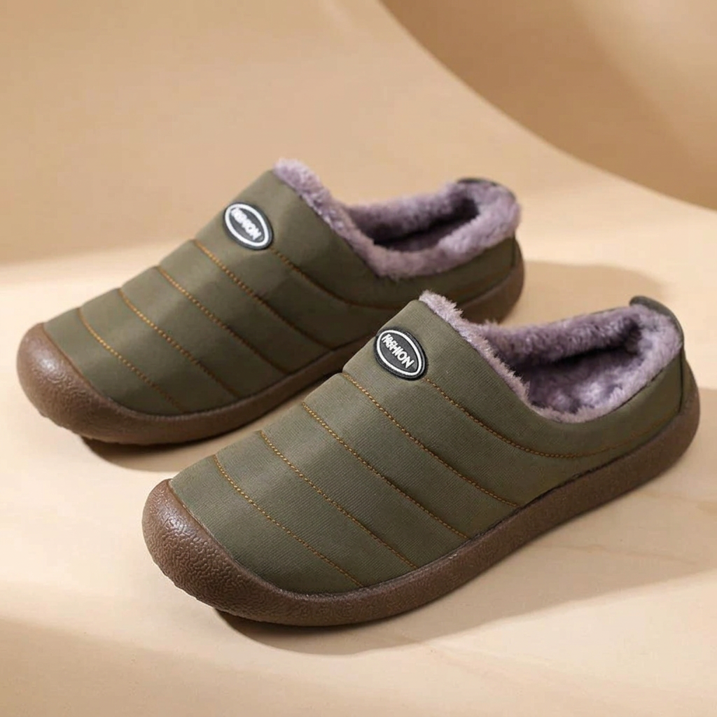Pair of olive green quilted slippers with purple-gray fleece lining on a beige curved backdrop 17