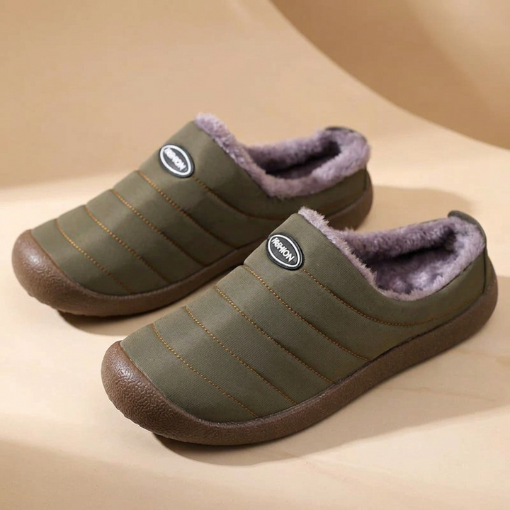 Pair of olive green quilted slippers with purple-gray fleece lining on a beige curved backdrop 17