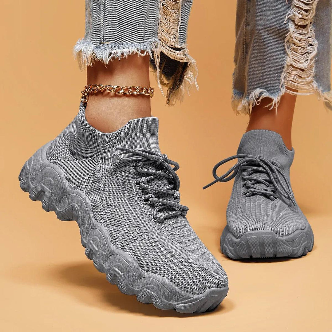 Model wearing solid gray knit lace-up sneakers with sock-like collars and thick wavy soles, gold anklet and frayed jeans visible. 46