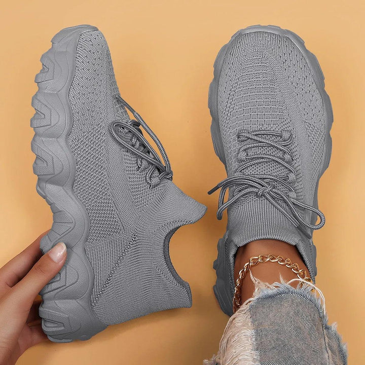 Overhead shot of solid gray knit sneakers, one held by hand to show the sole profile, the other worn with ripped jeans. 44