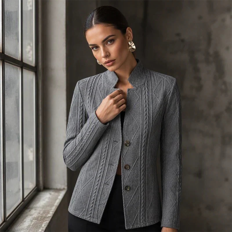 Gray textured blazer on a model standing by a window, hand at the collar, with large gold earrings 10
