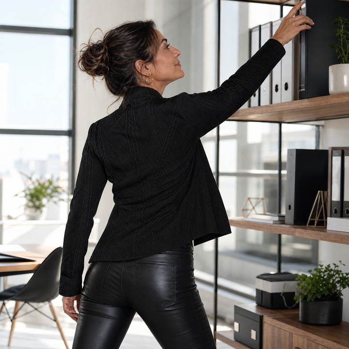 Back view of the black textured blazer on a woman reaching for binders on an office shelf, wearing leather pants 13