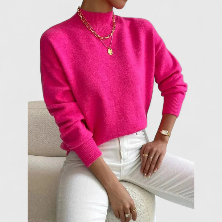 Women's sweater in bright hot pink with gold layered necklaces, a ribbed mock collar and white jeans.