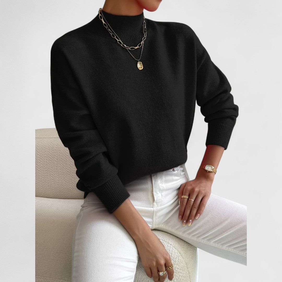 Women's sweater in black with a ribbed mock collar and cuffs, paired with white jeans and gold necklaces.