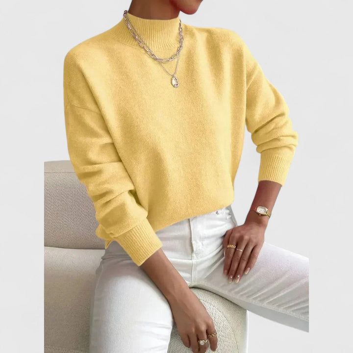 Women's sweater in pale yellow with a ribbed mock collar and cuffs, styled with white jeans and silver necklaces.