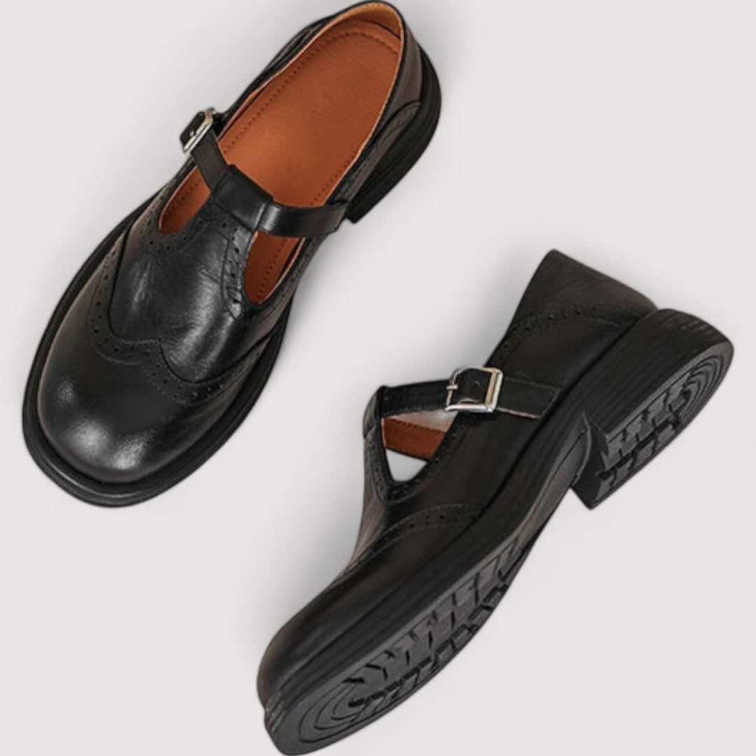 Flat lay of black leather Mary Janes: one shown from above with tan lining, the other turned to reveal the treaded rubber outsole. 5