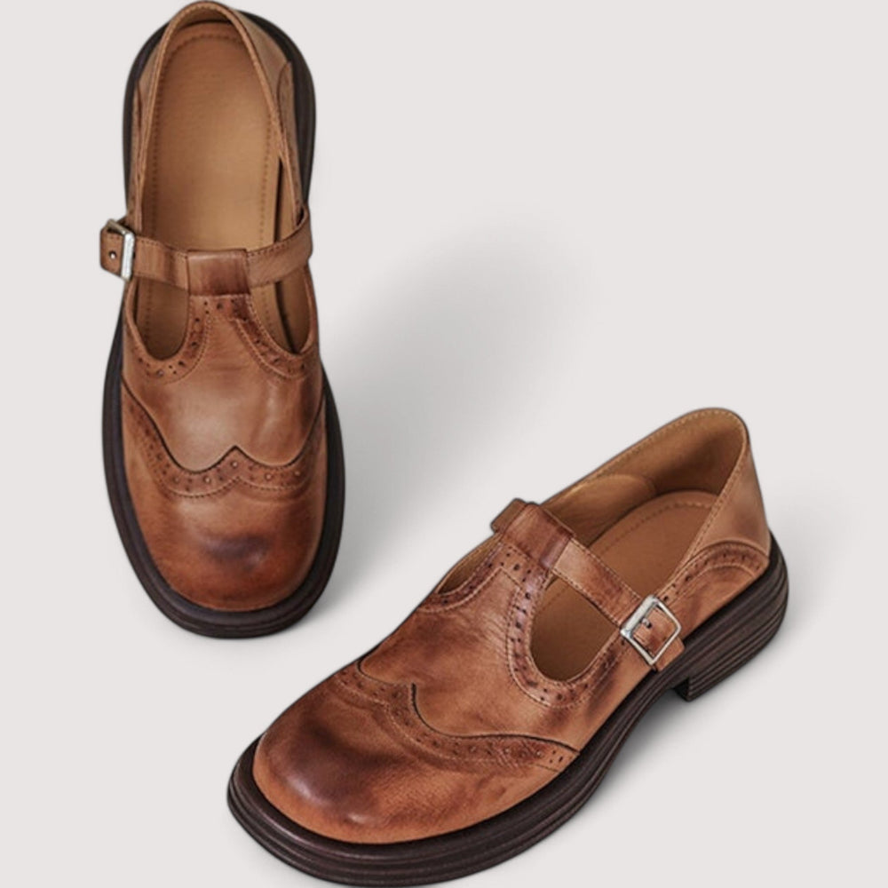 Pair of brown leather brogue Mary Janes seen from above and the side, showing perforated wingtip detail, buckle strap and tan interior. 2