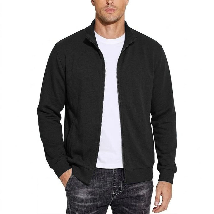 Man wearing the black stand-collar zip jacket open over a white tee and dark faded jeans, front view with one hand in pocket. 1