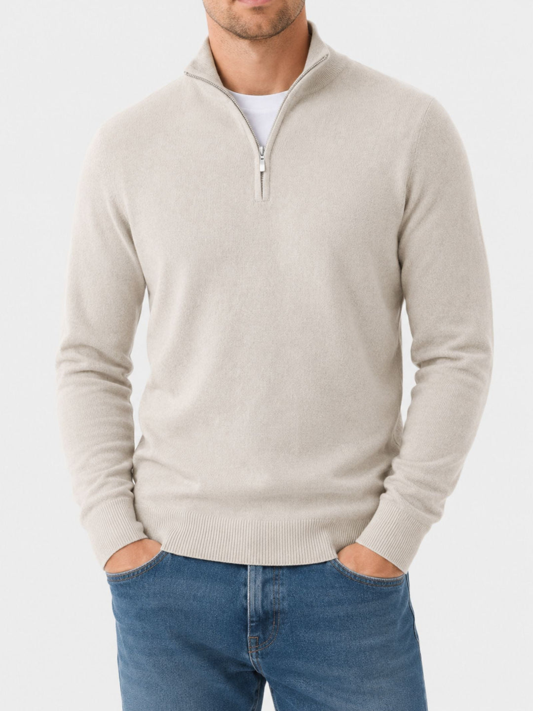 Close front view of a model in a cream quarter-zip knit sweater with both hands in jeans pockets, face cropped.