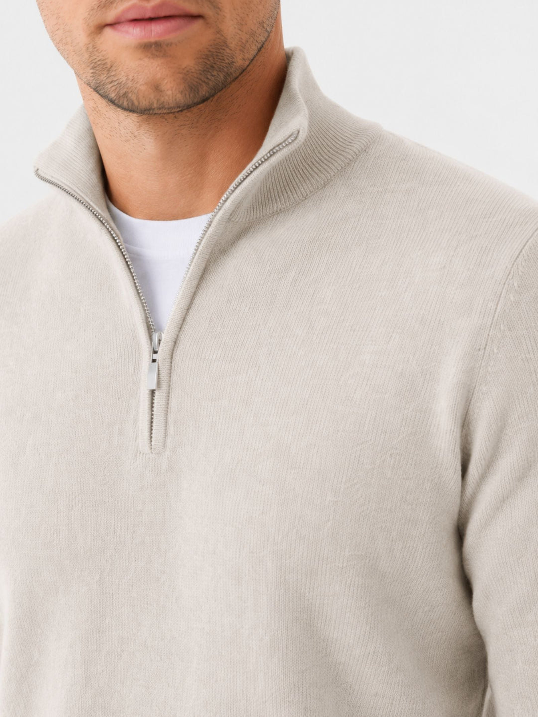 Close-up of the cream sweater's stand collar and silver zipper pull on a model, white tee visible underneath.