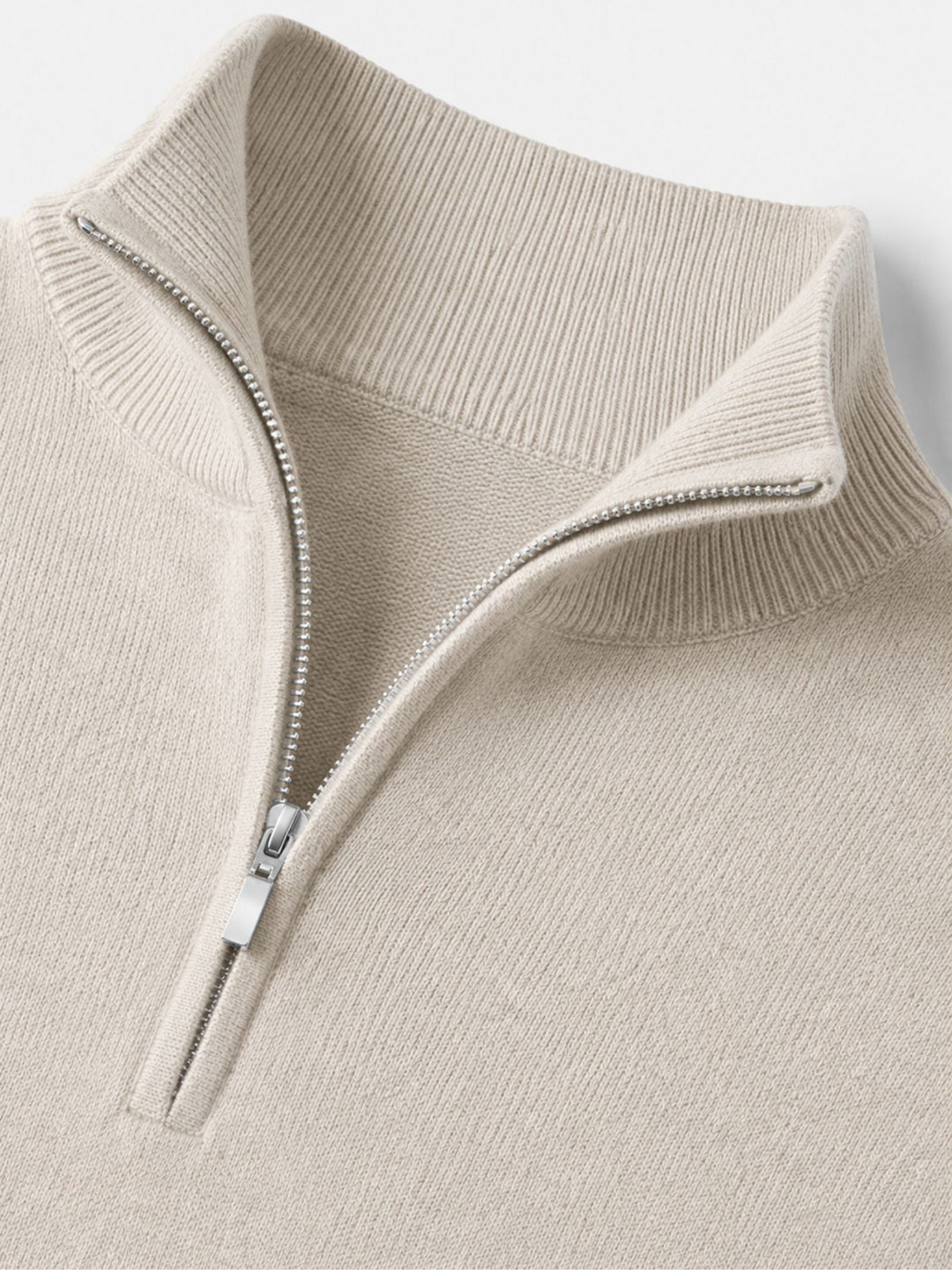 Detail of the cream sweater's ribbed stand collar and silver quarter-zip with metal zipper pull.