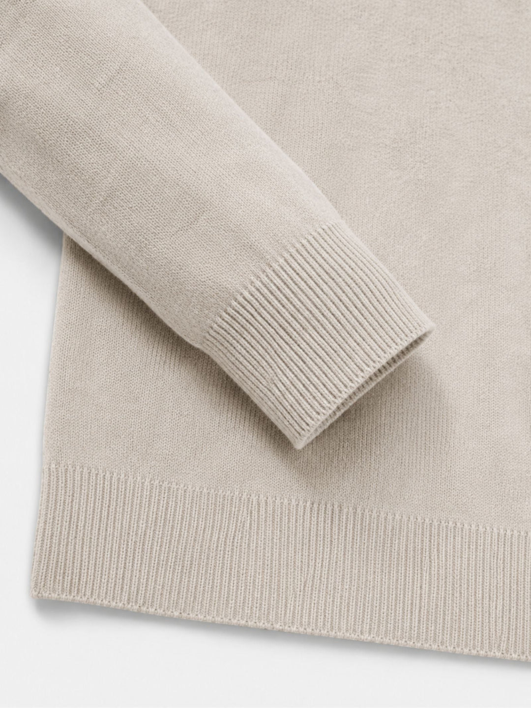 Detail of the cream sweater's ribbed cuff and ribbed bottom hem, laid flat to show the knit texture.