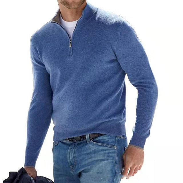 Man wearing the quarter-zip knit sweater in blue, white tee underneath, with jeans and a dark jacket in hand.