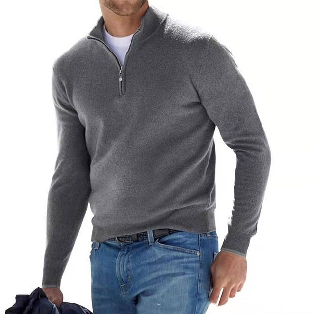 Man in a gray quarter-zip knit sweater, worn with a white tee, jeans and a belt.